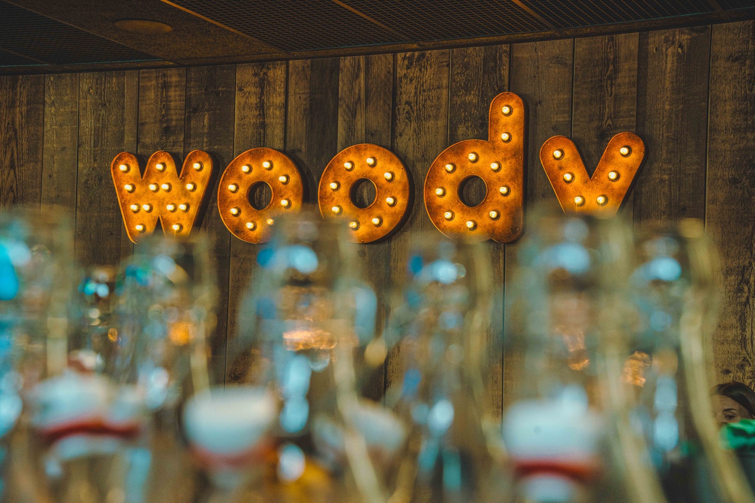 Enseigne lumineuse Woody avec lettres métalliques rétro-éclairées par ampoules, fixée sur un mur en bois