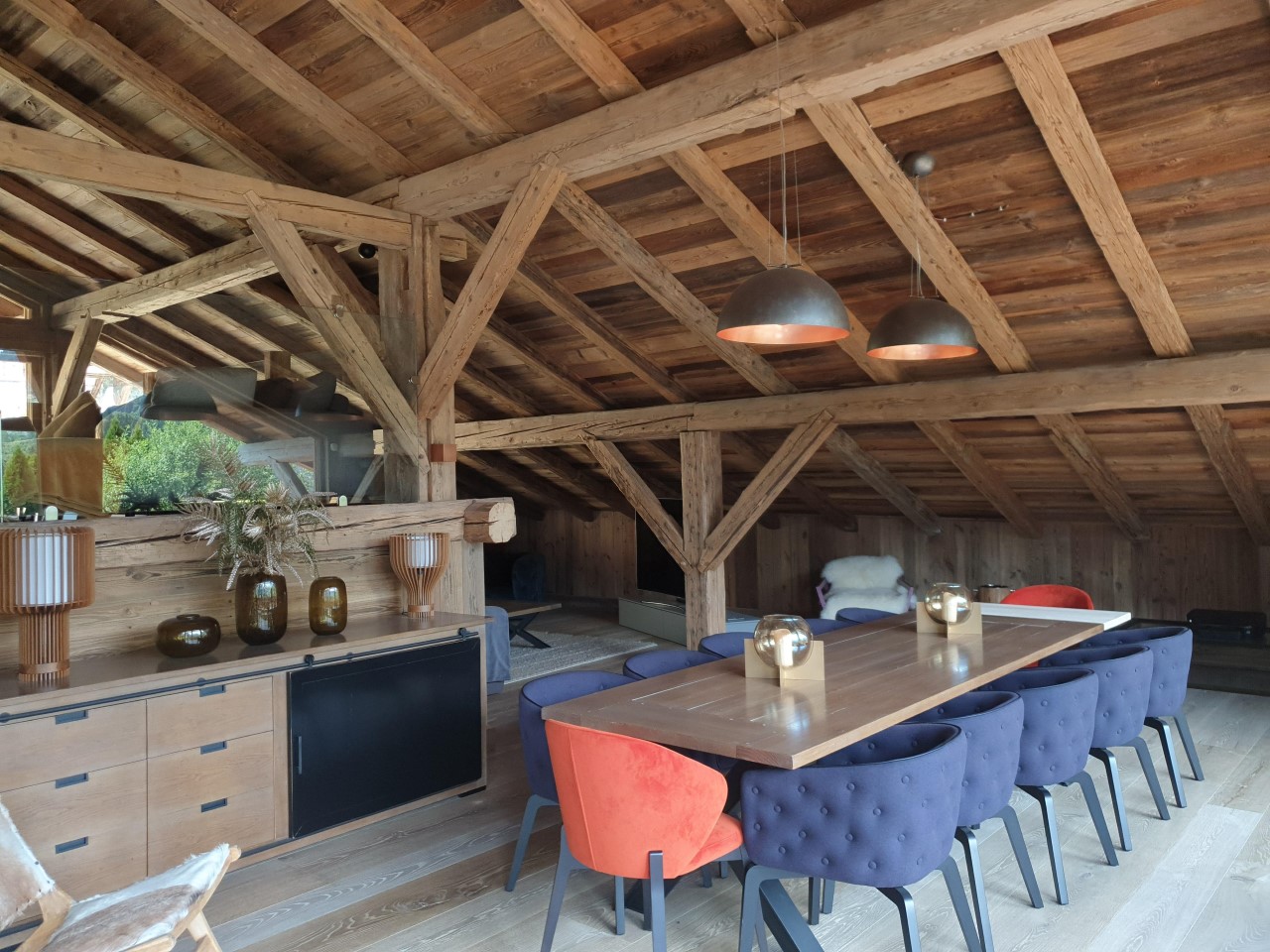 Installation électrique dans un chalet à Morzine : luminaires suspendus au-dessus d’une grande table à manger sous charpente en bois apparente