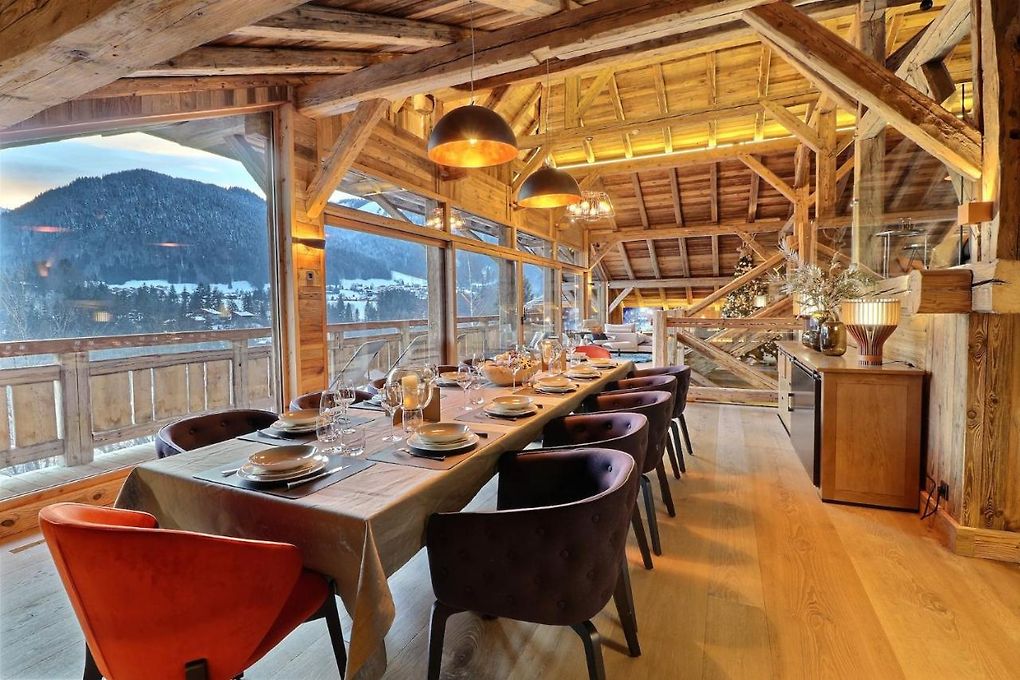 Salle à manger d’un chalet à Morzine avec éclairage chaleureux, poutres apparentes et vue sur les montagnes enneigées